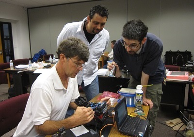 Phil Graham works on a fusion splice while Luis Torres (left) from District 10 and Michael Mullen (holding a light) from District 3 watch and talk through the exercise with Phil.