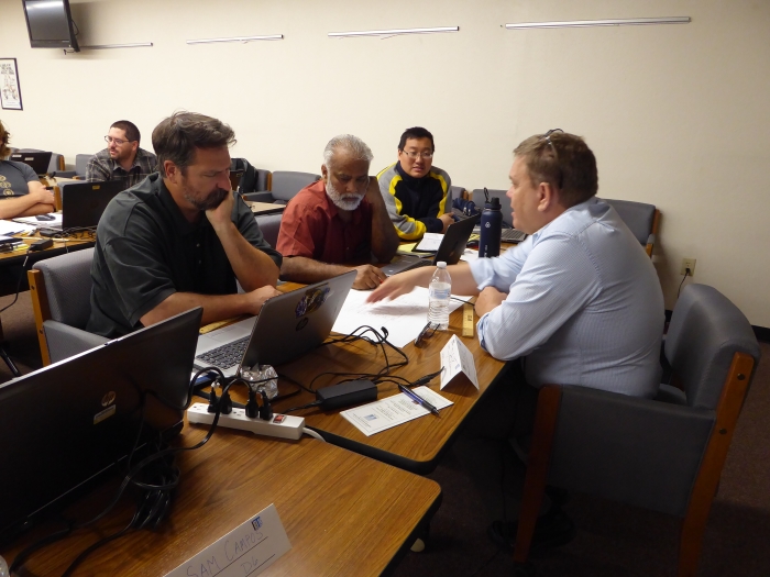 Students from Caltrans District 3 discuss their lab work with the course instructor. (Left to Right: David Busler, Gurdeep Sidhu, Andrew Chang, Phil Isaak) Three students face an instructor across a table. The instructor is pointing at papers on the table and talking.