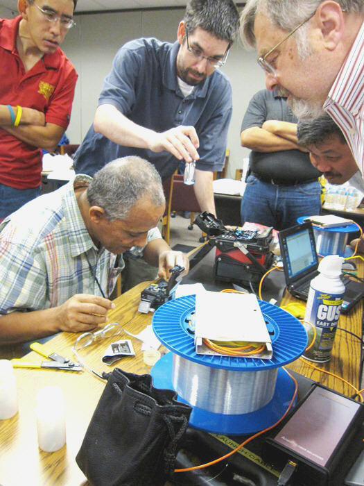Berhanu Zergaw works carefully on a fusion splice while the instructor observes his work.  Other students gathered around to watch.  Clockwise from left:  Steven Gee, Michael Mullen, Dave Le, Eric Pearson. (Mastering Fiber Optic Network Design and Installation, 2012)
