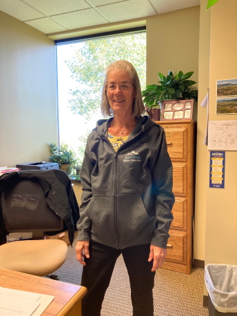 A woman stands in an office wearing a Western States Forum zippered hoodie sweatshirt