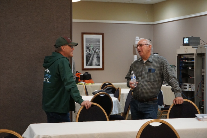 Two men standing facing each other, ITS cabinet in the background.