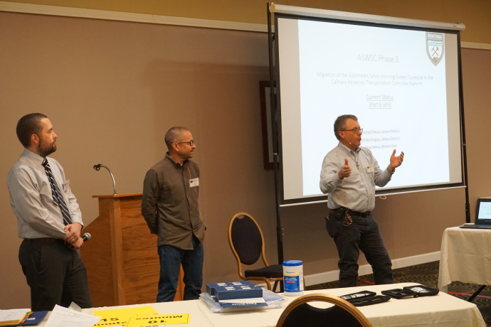 Three speakers present next to a projector screen