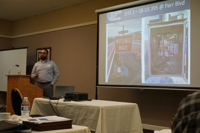 Rick Tydeman Man speaking next to a projector screen displaying a wrong way sign and the inside of a controller cabinet, slide text: Site 1 - SB US 395 @ Parr Blvd