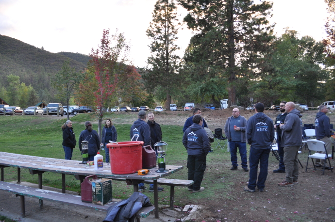 A group of people wearing WSRTC sweatshirts standing and visiting in a park with picnic tables