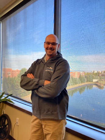 Neil Hetherington A man stands in an office wearing a Western States Forum zippered hoodie sweatshirt