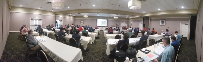 Meeting room during technical presentations. Group of people at tables listening to a speaker in the front of the room