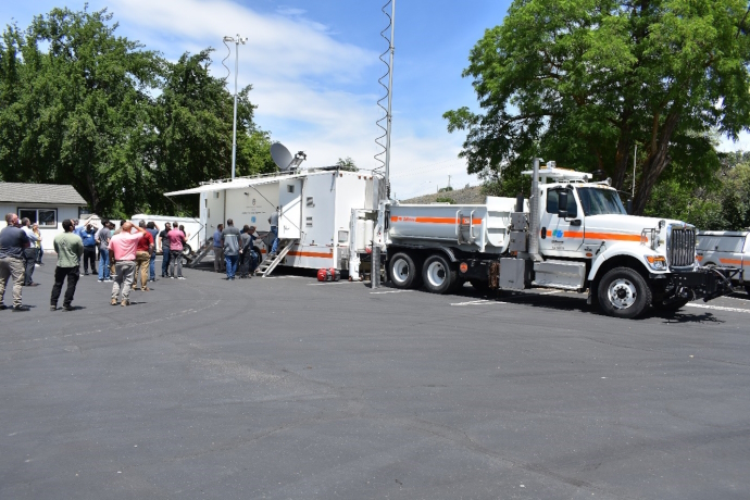 Caltrans Satellite Communications Truck and Trailer deployed during the demonstration Caltrans satellite communications truck and trailer parked in a parking lot, antennas and dish deployed, a group of people looking at truck/trailer and entering trailer.