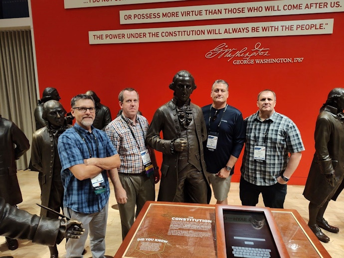WSRTC members at NRITS 2024 Several life-size statues with four men posing among them. In front is a display about the Constitution and on the wall behind is part of a quote from George Washington in 1787 – “or possess more virtue than those who will come after us. The power under the Constitution will always be with the people.”