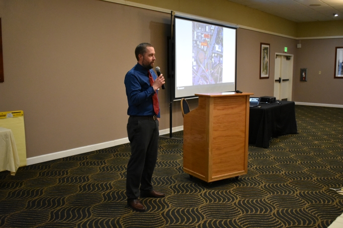 Jeremiah Pearce A man holds a microphone and speaks to an audience in front of a projector.