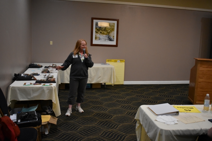Leann Koon A woman holds a microphone and speaks to an audience.