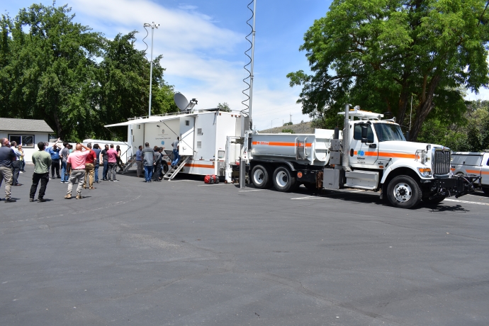 Caltrans District 1 mobile communications truck and trailer A line of people enters a large white trailer labeled 'Highway Emergency Response Center.' The trailer is located in a parking lot behind a large truck. Two antennas are deployed on either side of the trailer.