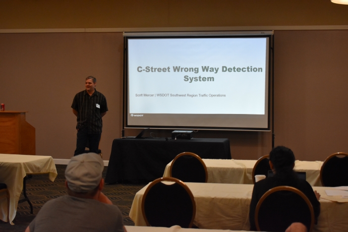 Scott Mercer A man stands to the left of a projector screen speaking to an audience. The screen is titled 'C-Street Wrong Way Detection System.'
