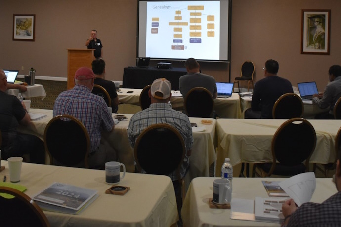 Doug Galarus explains OSS project history. A presenter behind a podium points to the audience in front of him.