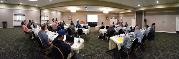 Meeting room during 2024 WSF technical presentations. Group of people sitting at tables arranged classroom style looking to the front where a person is speaking.