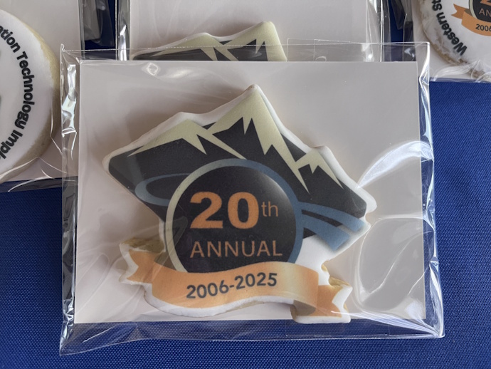 Cookie in a plastic sleeve, Forum mountain and road, 20th Annual, 2006-2025 ribbon; custom shaped cookie follows the outline of the mountain, badge, and banner.